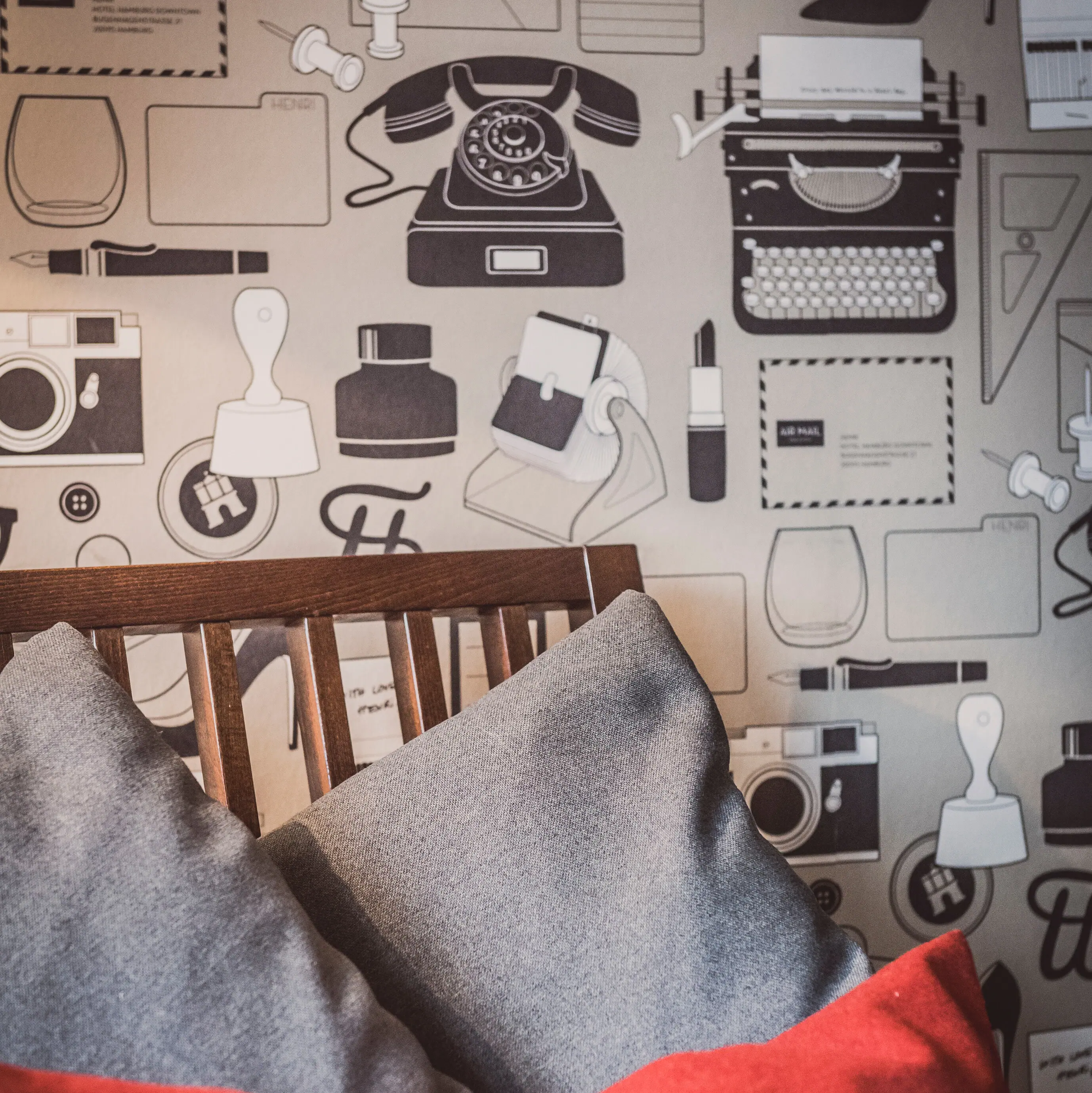 Sessel mit grauen und roten Kissen vor einer Wand mit Motivtapete