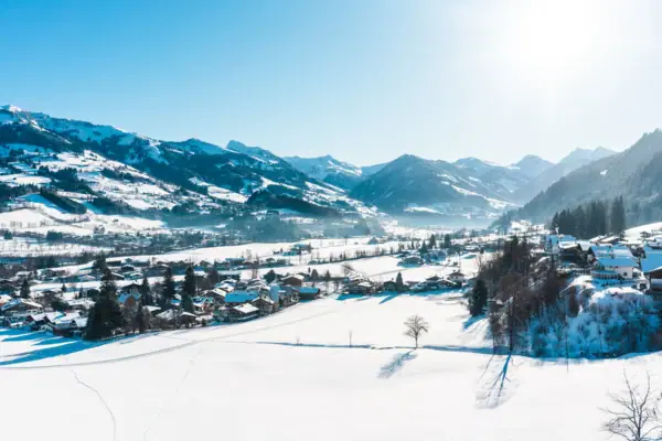Verschneite Landschaft mit einem Dorf und Bergen im Hintergrund.