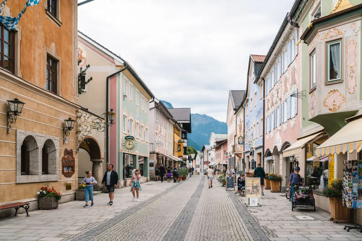 Ortszentrum Garmisch-Partenkirchen Straße mit Gebäuden und Menschen, die spazieren gehen.