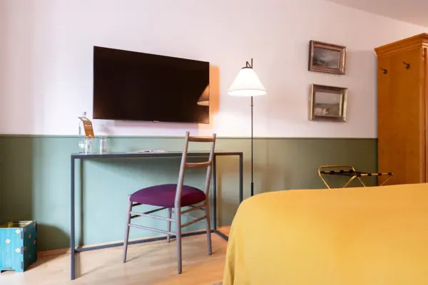 Hotelzimmer HENRI Hotel Garmisch-Partenkirchen Ein Hotelzimmer im HENRI Hotel Garmisch-Partenkirchen mit einem Schreibtisch und einem Fernseher an der Wand.