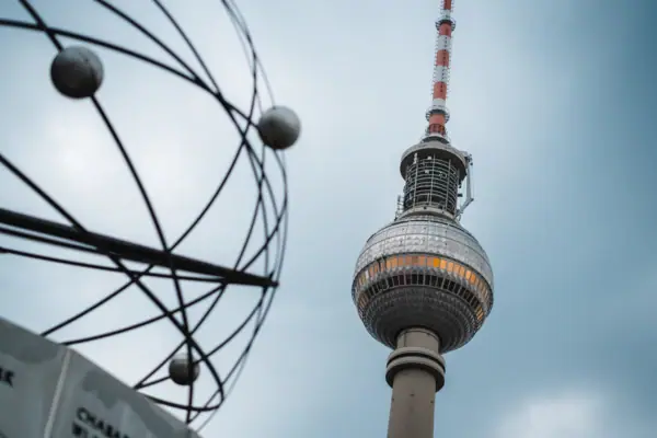 Der Berliner Alexanderplatz mit hohem runden Turm vor blauem Himmel mit Wolken.