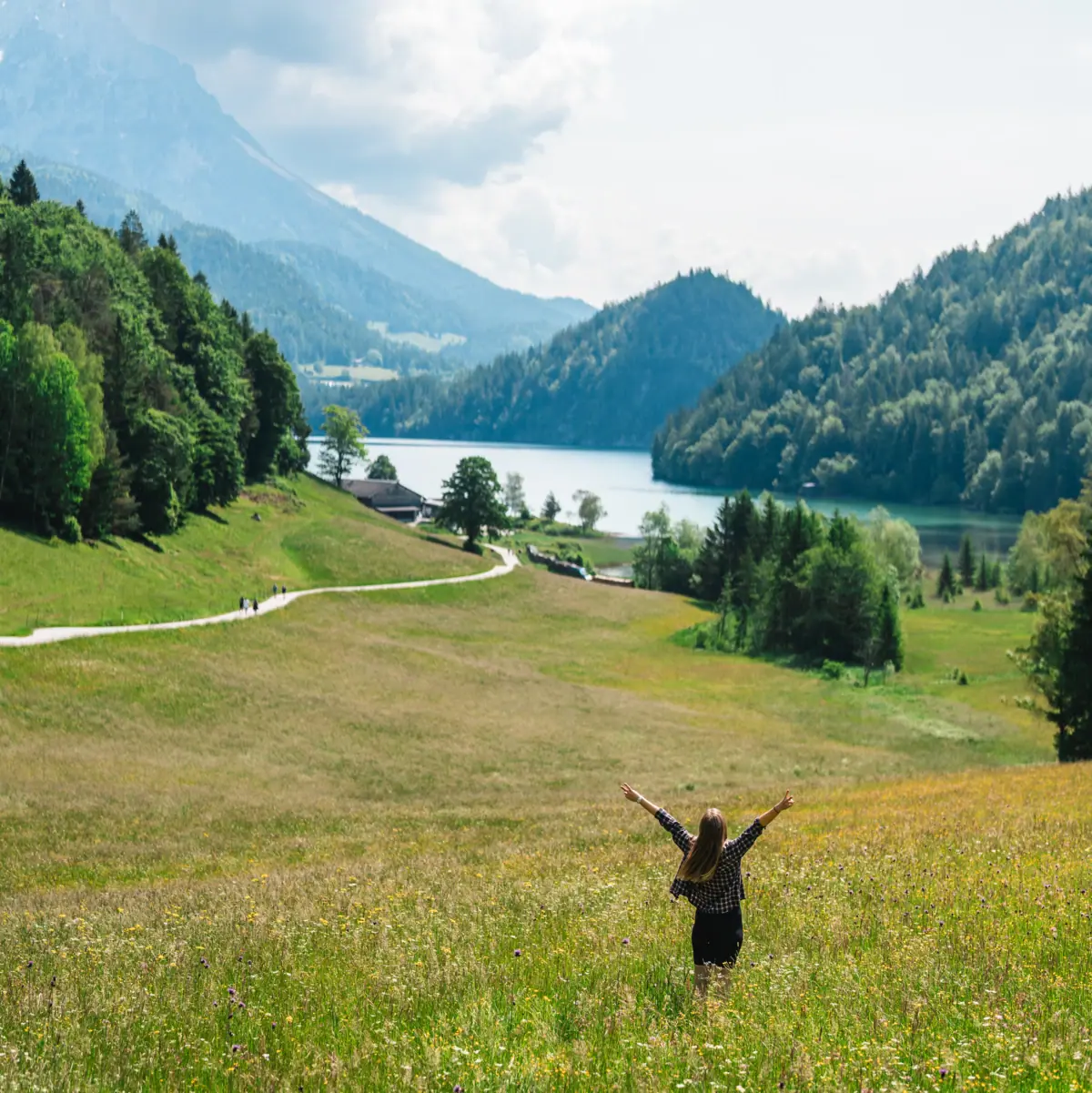 Frau steht auf den Almwiesen und blickt auf den See und die Berge.