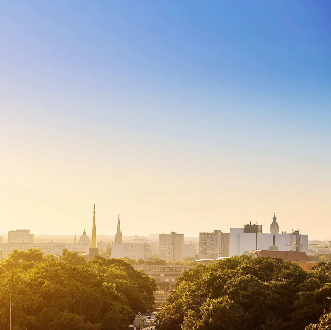 Stadt-Skyline mit Bäumen im Vordergrund und klarem Himmel im Hintergrund.