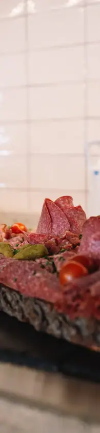 Rustic wooden platter with a variety of sliced cured meats, presented on a wooden table alongside bread and cutlery.