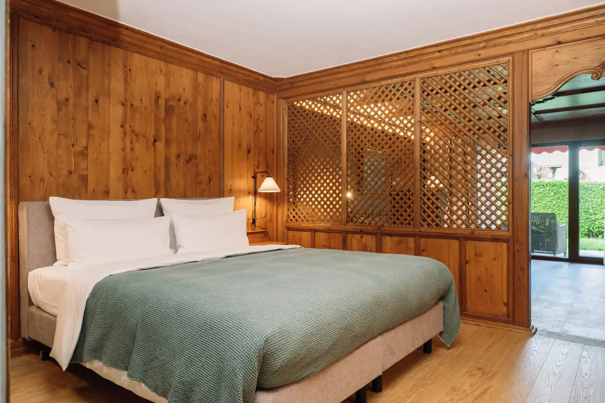 Ein Bett mit grüner Decke vor einer holzgetäfelten Wand.