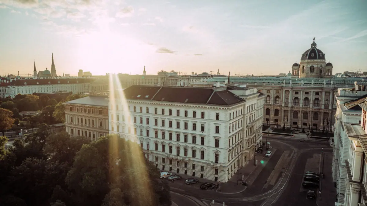 Blick über Wien Ein großes weißes Gebäude mit vielen Fenstern und einer Straße im Vordergrund, umgeben von Bäumen.