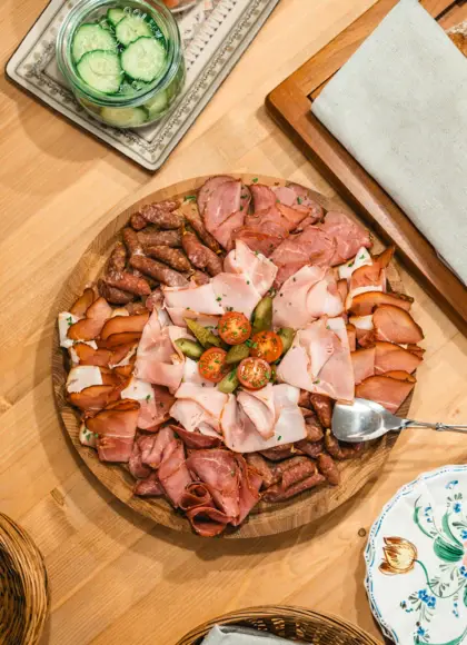 Rustic wooden platter with a variety of sliced cured meats, presented on a wooden table alongside bread and cutlery.