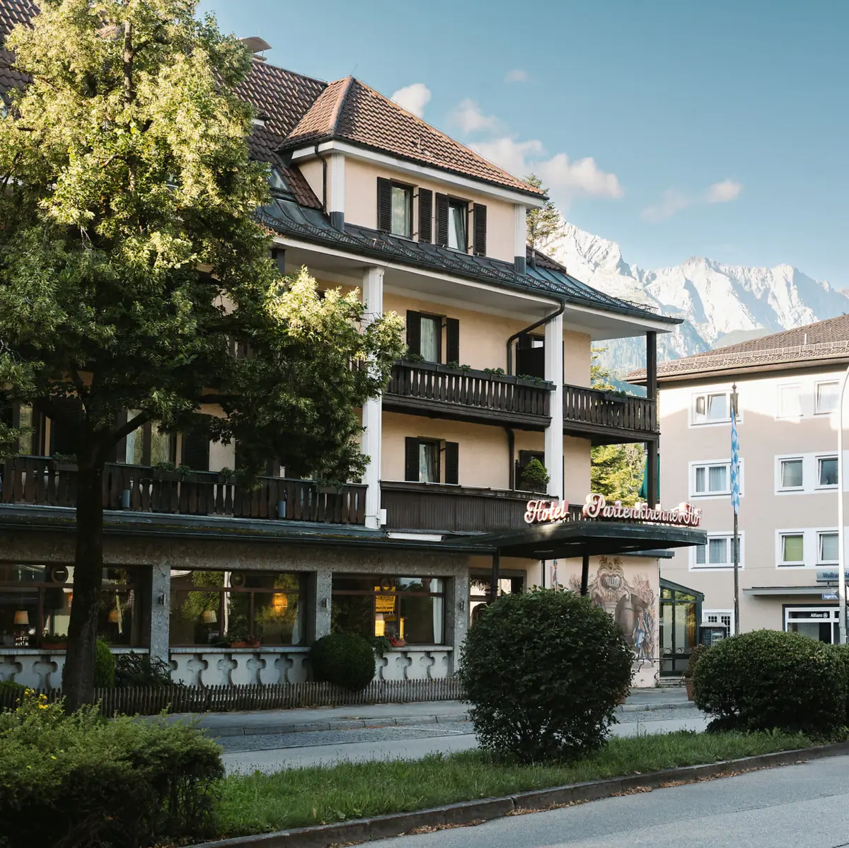 Das HENRI Hotel in Garmisch-Partenlkirchen mit Bäumen am Straßenrand und Bergen im Hintergrund.