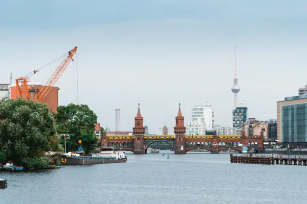 Ansicht der backsteingotischen Oberbaumbrücke in Berlin mit einer gelben U-Bahn und dem Berliner Fernsehturm im Hintergrund unter bewölktem Himmel