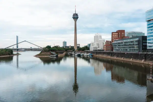 Die Skyline von Düsseldorf mit einem Fluss im Vordergrund und einem Turm im Hintergrund.