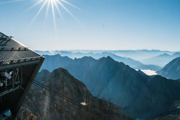 Der Ausblick von der Zugspitze mit Bergkette, Seilbahn und strahlender Sonne.