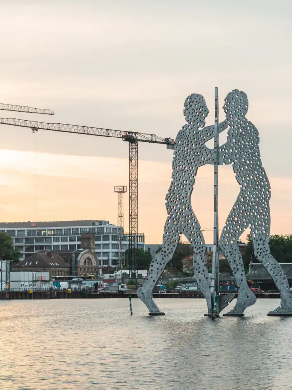 Große Metallsäule von Männern im Wasser mit Kränen im Hintergrund.