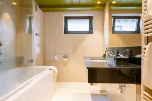 Badezimmer Suite im HENRI Garmisch-Partenkirchen Badezimmer mit Waschbecken und Badewanne, ausgestattet mit Armaturen und Spiegel.