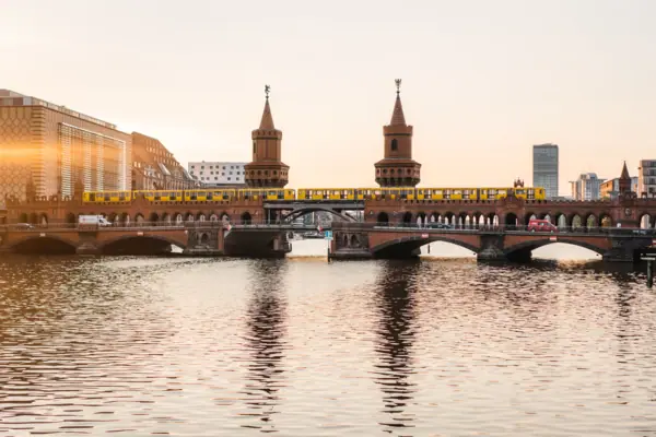 Ansicht der backsteingotischen Oberbaumbrücke in Berlin bei Sonnenuntergang mit einer gelben U-Bahn und Spiegelung im Wasser.