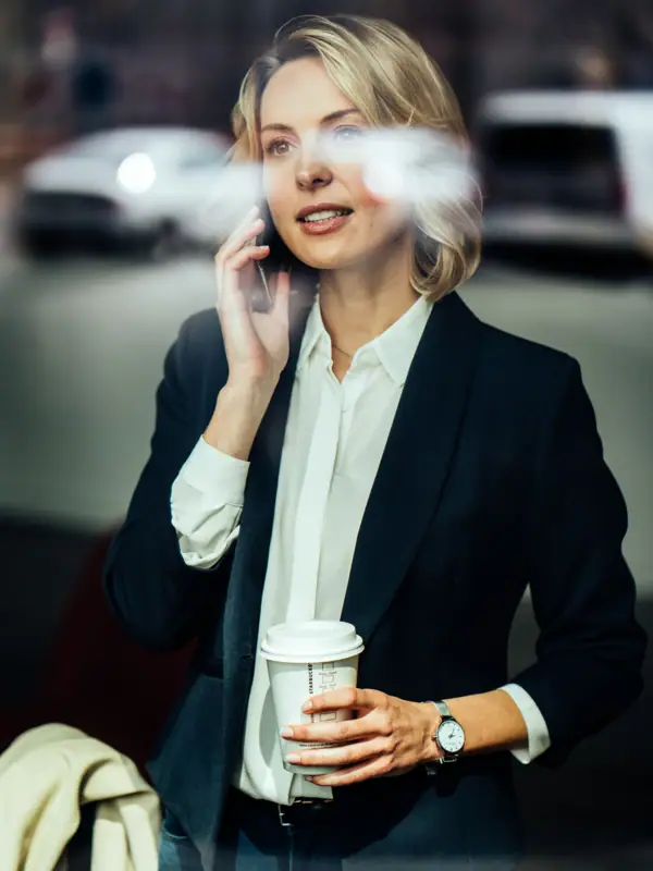 Frau hält einen Kaffeebecher und telefoniert.