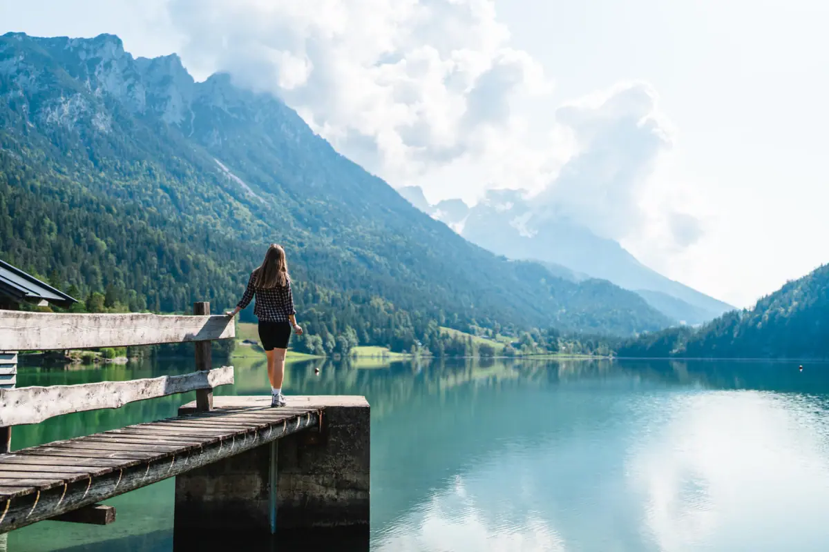 Eine Frau steht auf einem Steg und blickt auf einen See.