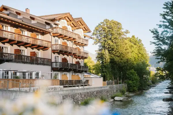 HENRI Kitzbühel Ein Gebäude mit Balkonen und einem Fluss im Vordergrund.