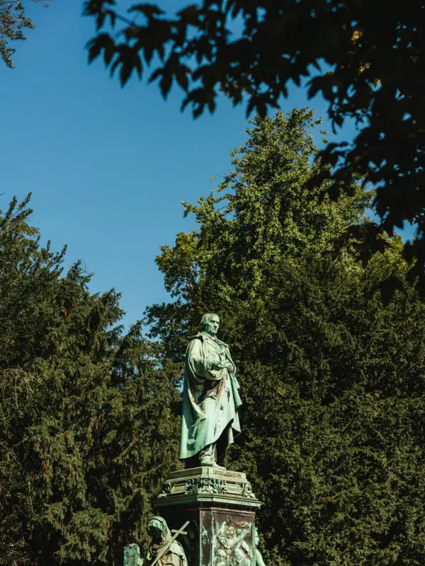 Statue eines Mannes in einem Gewand im Freien vor blauem Himmel.