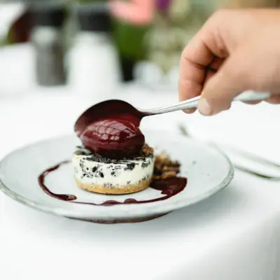 Hand hält einen Löffel über ein Dessert.