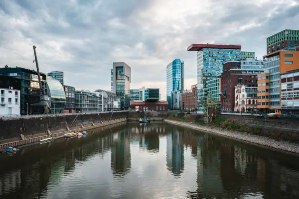 Düsseldorf Fluss mit Gebäuden im Hintergrund und bewölktem Himmel.