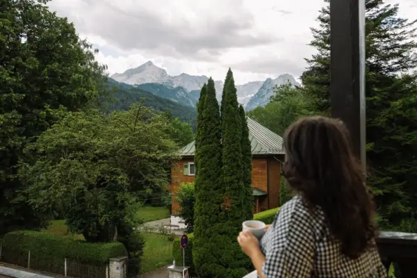 Eine Frau hält eine Tasse Kaffee und blickt auf ein Bergpanorama.