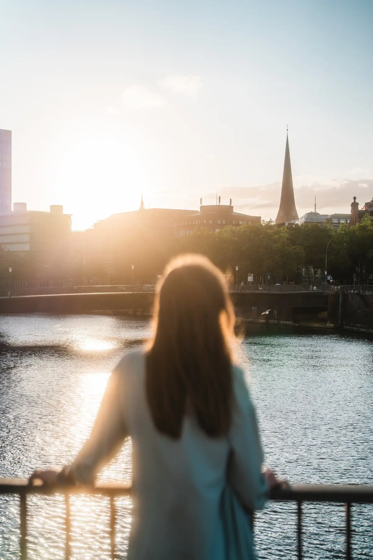 Eine Frau steht auf einer Brücke und blickt auf eine Stadt.