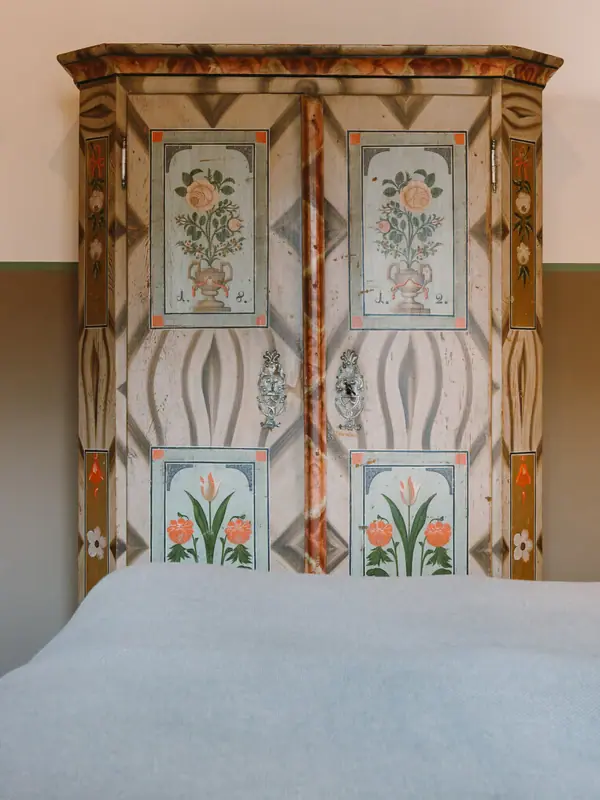 Ein Bett mit bemaltem Schrank im Hintergrund.