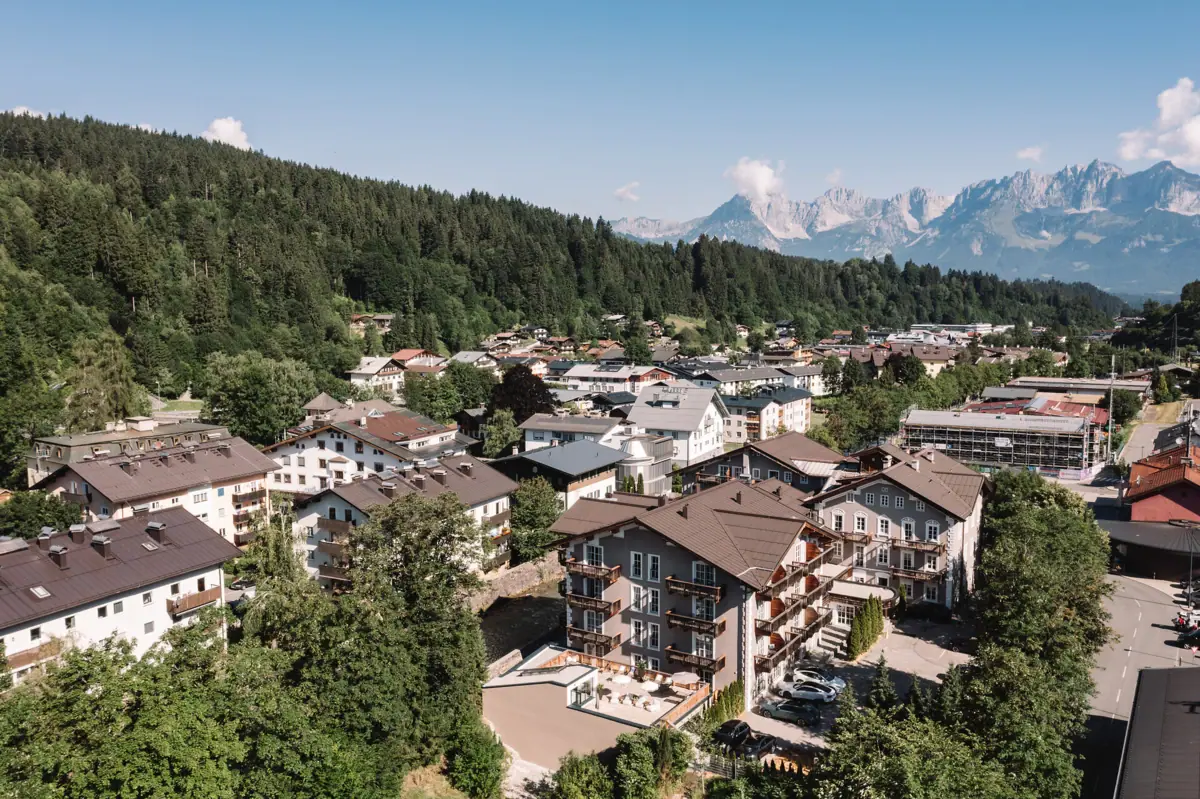 HENRI Hotel Kitzbühel Eine Gruppe von Gebäuden mit Bäumen und Bergen im Hintergrund.