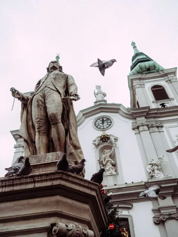 Haydnstatue Wien Statue eines Mannes mit fliegenden Tauben im Freien vor einem klaren Himmel.
