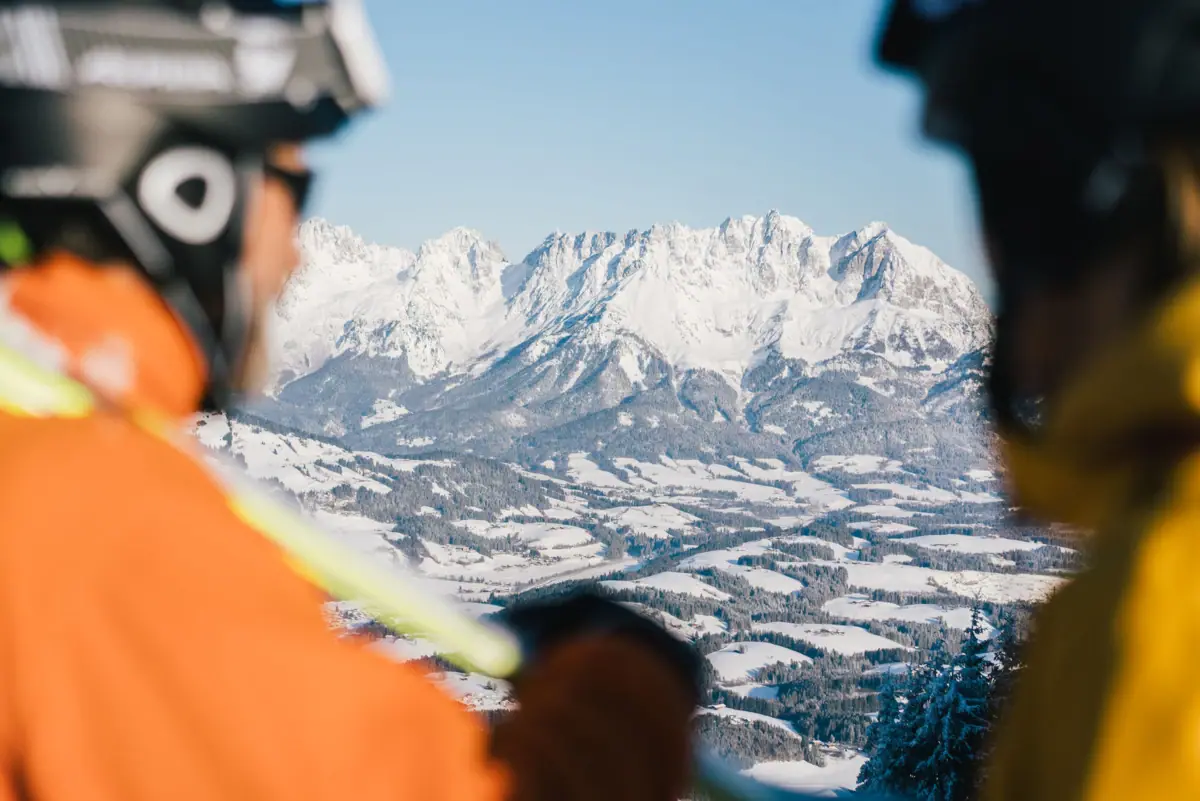 Eine Gruppe von Menschen auf einer Skipiste blickt auf einen verschneiten Berg.