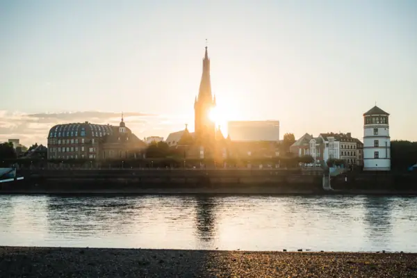 Rheinuferpromenade Düsseldorf Stadtansicht mit einem hohen Turm und einem Gewässer im Vordergrund.