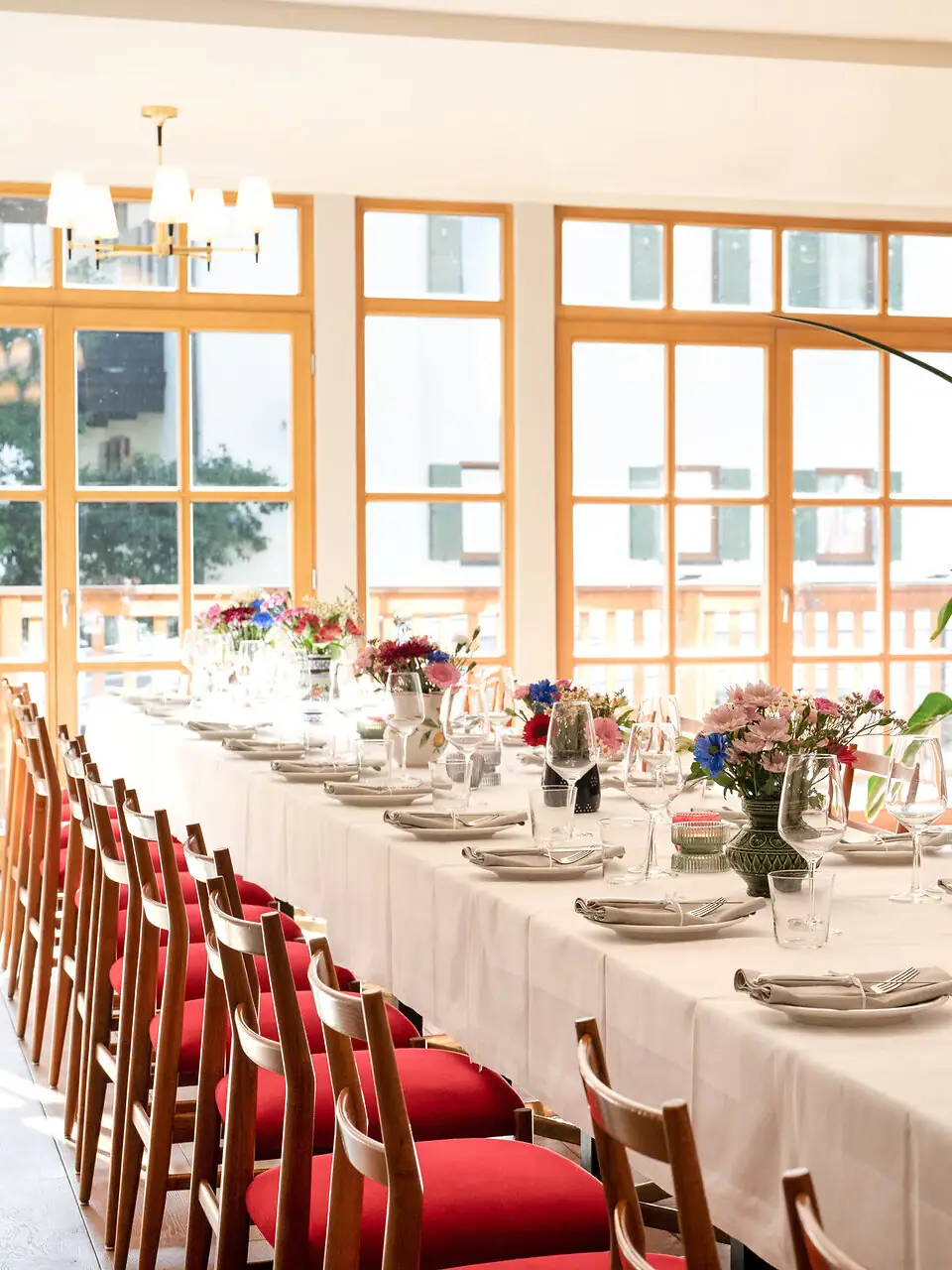 Langer Tisch mit weißem Tischtuch und Blumen darauf.