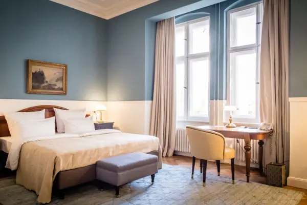 HENRI Hotel Berlin Design Zimmer Blau mit Schreibtisch Stilvolles Hotelzimmer im HENRI Berlin mit hellblauen Wänden, einem Doppelbett, antikem Holzschreibtisch und hohen Fenstern im klassischen Altbau-Design.