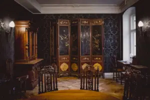 HENRI Hotel Berlin Salon Interieur mit Paravent Ein prachtvoll gestalteter Salon im HENRI Berlin mit dunkler Mustertapete, einem antiken mehrteiligen Paravent mit Goldmalerei und herrschaftlichen Holzmöbeln.