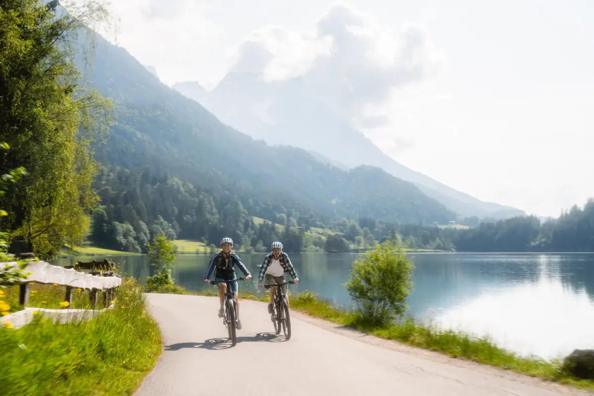 Mountainbike Kitzbühel Zwei Personen fahren mit Fahrrädern auf einer Straße in der Nähe eines Sees in Kitzbühel.