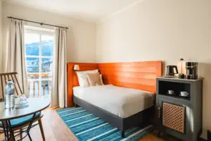 Einzelbett mit Terrassentür und kleinem Tisch.