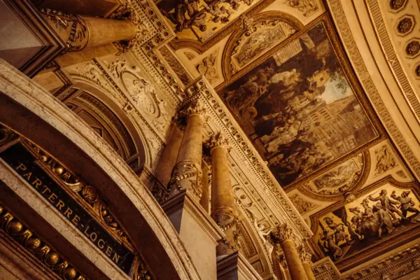 Burgtheater Wien Decke mit Säulen und Gemälden, symmetrisch gestaltet und kunstvoll verziert.