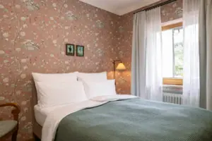 HENRI GAP Petit Kabinett Bett mit grünem Überwurf und Lampe vor floralem Tapetenhintergrund.