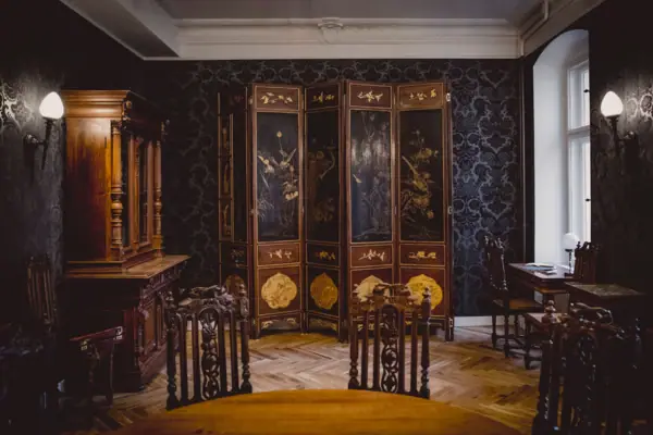 HENRI Hotel Berlin Salon Interieur mit Paravent Ein prachtvoll gestalteter Salon im HENRI Berlin mit dunkler Mustertapete, einem antiken mehrteiligen Paravent mit Goldmalerei und herrschaftlichen Holzmöbeln.