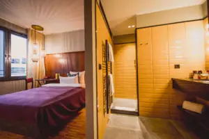 Das S-Studio im HENRI Hotel Düsseldorf mit einem Bett und einem angrenzendem Bad mit einem Waschbecken und einer Dusche.