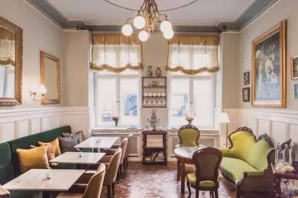 HENRI Hotel Berlin Salon Interieur Klassisch Ein heller, klassisch gestalteter Salon im HENRI Berlin mit grünen Samtsofas, Marmortischen, einem antiken Samowar und herrschaftlichen Ölgemälden an den Wänden.