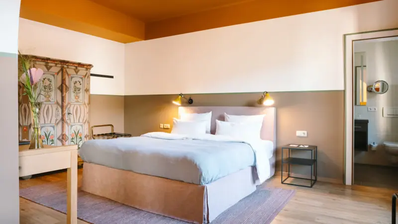 Ein Hotelzimmer im HENRI Hotel Garmisch-Partenkirchen mit einem gemütlichen Bett und einem alten Schrank.