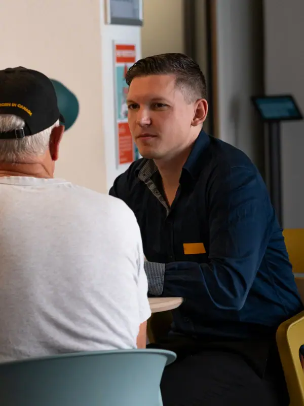 Ein Mann sitzt mit einem anderen Mann im weißen Hemd an einem Tisch.