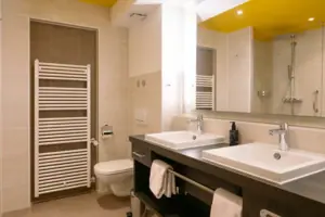 Badezimmer im HENRI Garmisch-Partenkirchen Badezimmer mit gelber Decke, Waschbecken und Armaturen.