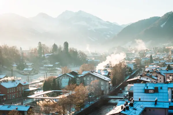 Schneebedeckte Dächer einer Stadt mit Bergen im Hintergrund.
