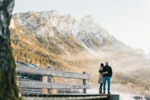Ein Mann und eine Frau stehen auf einem Steg mit Blick auf eine Bergkette.
