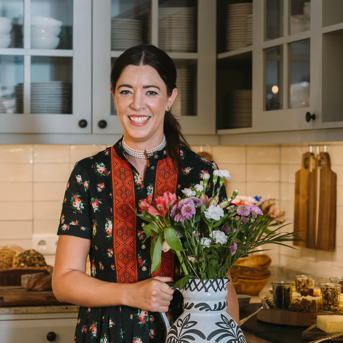 Hoteldirektorin Susanne mit einem Strauß Blumen in der Hausküche, im Hintergrund verschiedene Speisen.