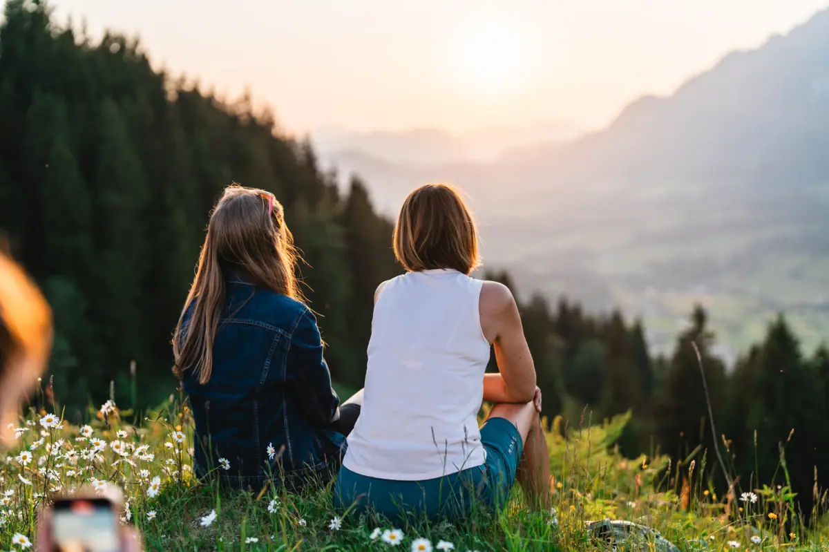 Ausblick Kitzbüheler Alpen Zwei Frauen sitzen auf einem Hügel und betrachten den Sonnenuntergang.