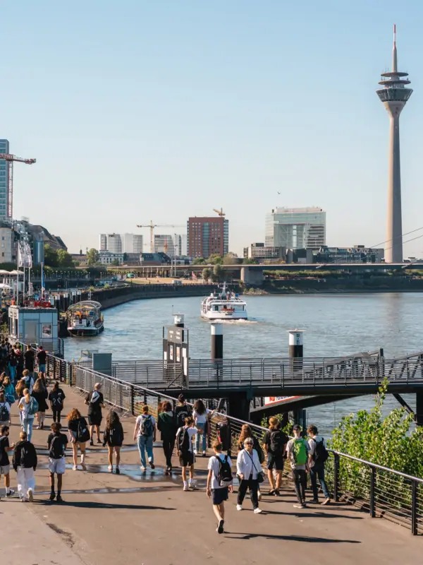 Rheinuferpromenade Düsseldorf Eine Gruppe von Menschen spaziert auf einem Weg in der Nähe von Wasser.