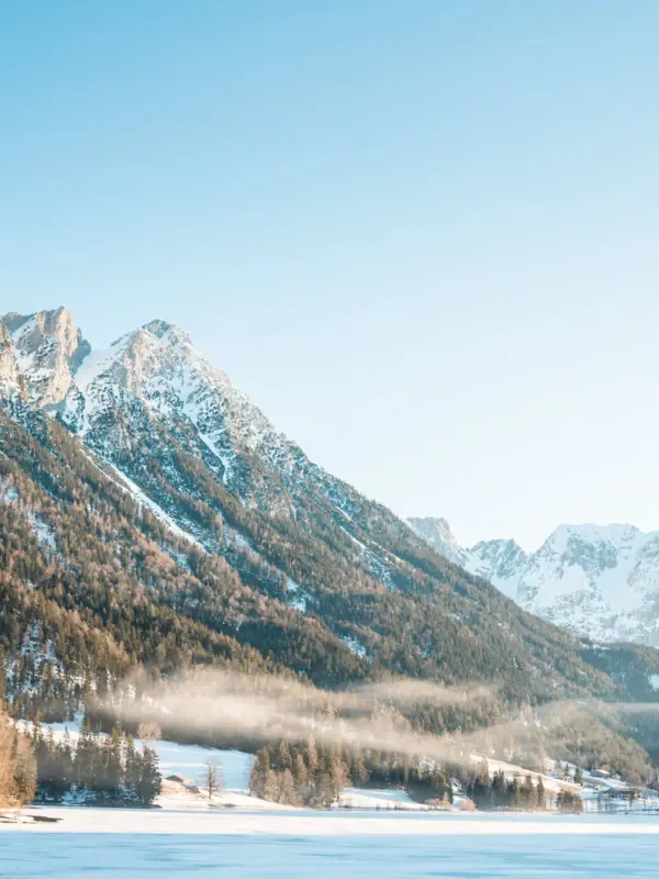 Verschneiter Berg mit Bäumen und einem Gewässer im Vordergrund.